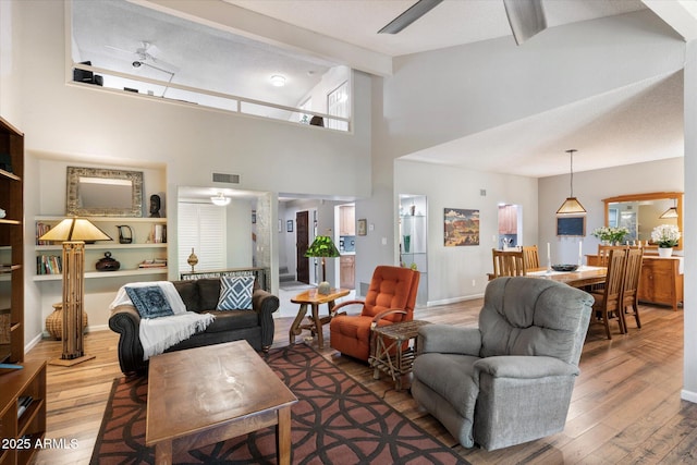 living room featuring ceiling fan, a towering ceiling, and hardwood / wood-style floors