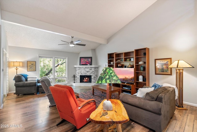 living room with ceiling fan, wood-type flooring, lofted ceiling with beams, and a stone fireplace