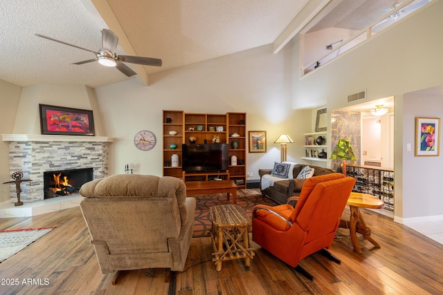 living room with ceiling fan, beam ceiling, light hardwood / wood-style flooring, and a tile fireplace