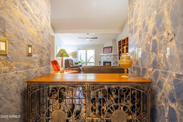 interior space with ceiling fan, tile walls, vaulted ceiling with beams, and a stone fireplace