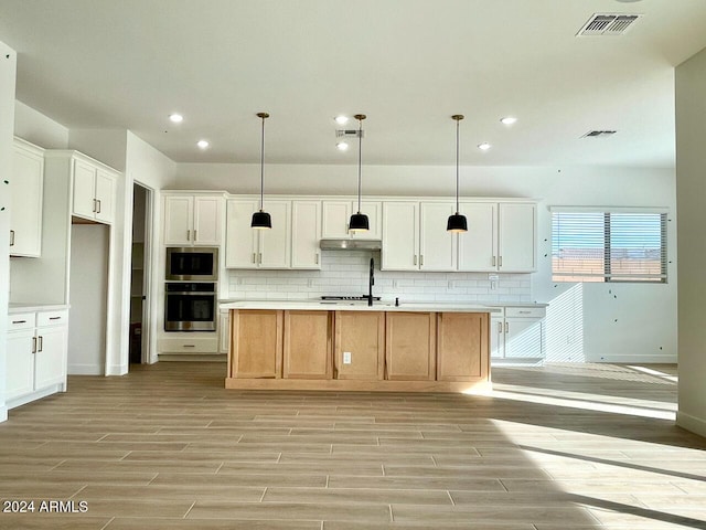 kitchen featuring appliances with stainless steel finishes, a kitchen island with sink, white cabinets, and decorative light fixtures