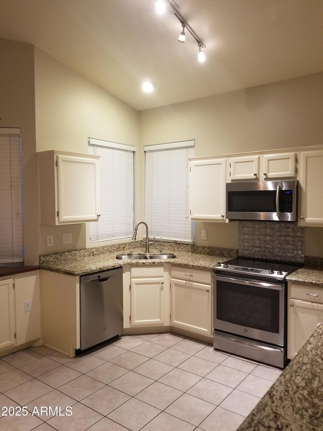 kitchen with lofted ceiling, sink, light stone counters, light tile patterned floors, and stainless steel appliances