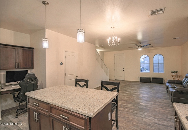 kitchen featuring dark hardwood / wood-style floors, hanging light fixtures, a center island, a kitchen bar, and ceiling fan with notable chandelier