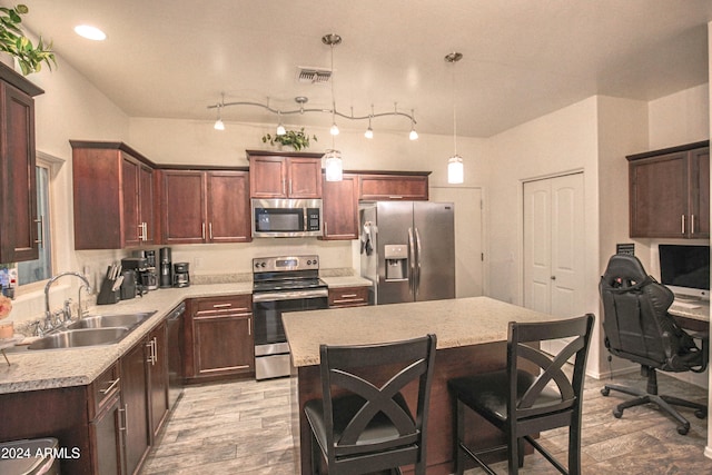 kitchen with appliances with stainless steel finishes, sink, a center island, decorative light fixtures, and light hardwood / wood-style flooring