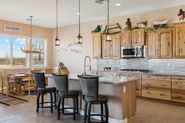 kitchen featuring appliances with stainless steel finishes, backsplash, a center island with sink, and light stone counters