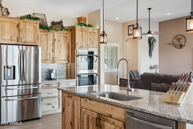 kitchen with appliances with stainless steel finishes, pendant lighting, light stone counters, and sink