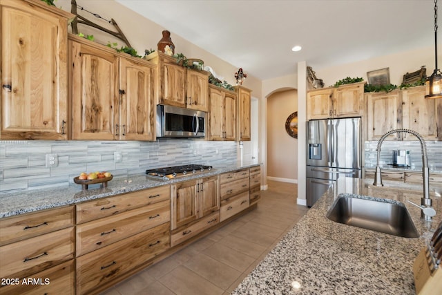 kitchen featuring decorative light fixtures, backsplash, sink, light stone countertops, and stainless steel appliances