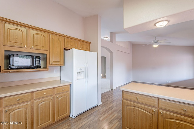 kitchen featuring ceiling fan, black microwave, light countertops, white fridge with ice dispenser, and arched walkways