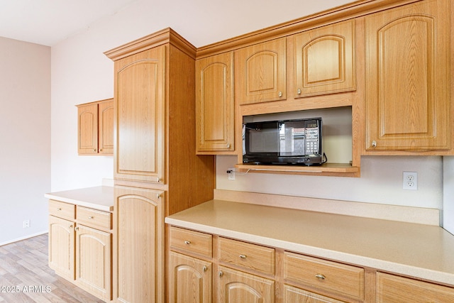 kitchen featuring light wood finished floors, light countertops, black microwave, and light brown cabinetry