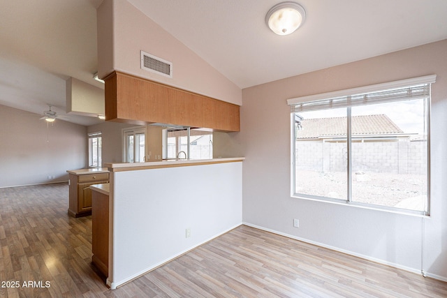 kitchen with visible vents, light wood finished floors, a peninsula, lofted ceiling, and ceiling fan