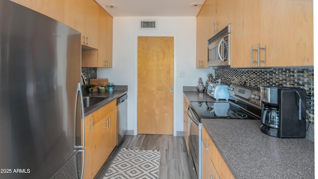 kitchen featuring tasteful backsplash, visible vents, dark countertops, stainless steel appliances, and a sink