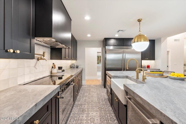 kitchen featuring wall chimney range hood, hanging light fixtures, backsplash, sink, and stainless steel appliances