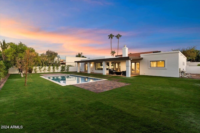 back house at dusk with a fenced in pool, a yard, and a patio