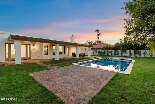 pool at dusk with a patio and a lawn