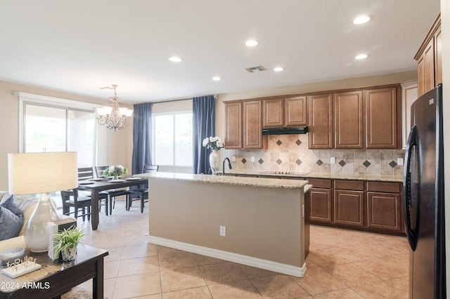 kitchen featuring a kitchen island with sink, black fridge, backsplash, pendant lighting, and light tile patterned floors