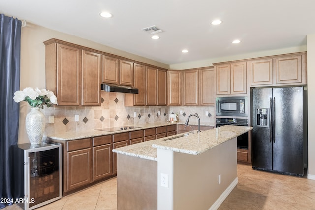 kitchen featuring wine cooler, tasteful backsplash, a center island with sink, black appliances, and light stone counters