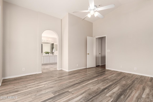 interior space with arched walkways, ensuite bath, wood finished floors, and high vaulted ceiling