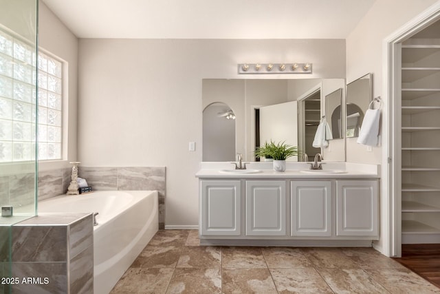 bathroom featuring double vanity, baseboards, a sink, and a bath