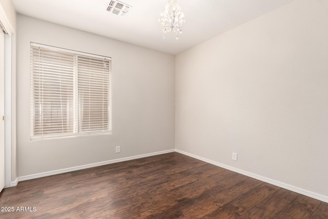 empty room featuring visible vents, dark wood-style flooring, baseboards, and a chandelier