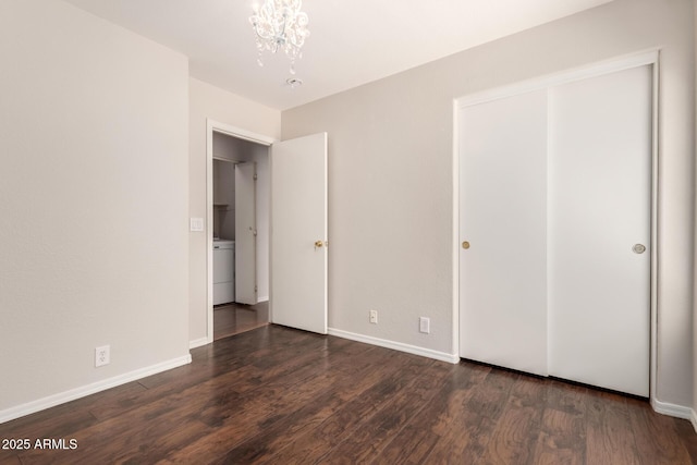 unfurnished bedroom featuring washer / dryer, baseboards, dark wood finished floors, and a chandelier