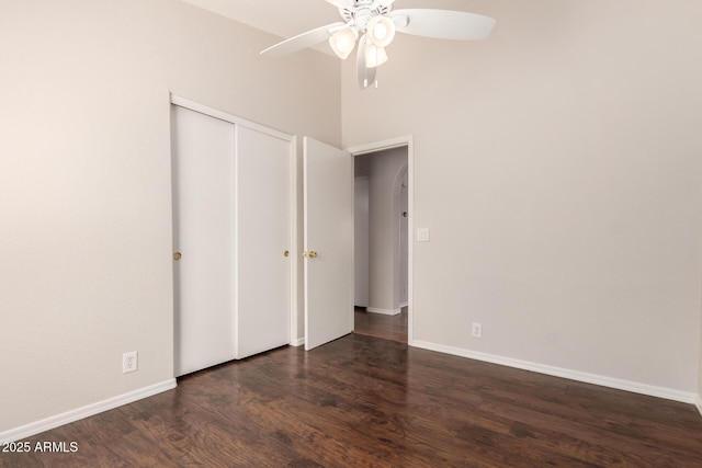 unfurnished bedroom featuring ceiling fan, a towering ceiling, wood finished floors, baseboards, and a closet