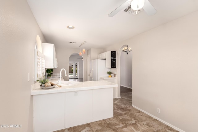 kitchen with arched walkways, tile counters, white fridge with ice dispenser, a ceiling fan, and visible vents