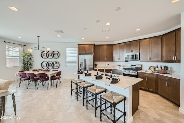 kitchen featuring a kitchen bar, sink, hanging light fixtures, a center island with sink, and stainless steel appliances