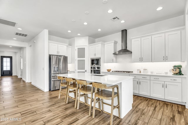 kitchen featuring wall chimney exhaust hood, appliances with stainless steel finishes, a sink, and visible vents