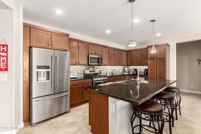 kitchen featuring an island with sink, sink, a kitchen bar, dark stone counters, and stainless steel appliances