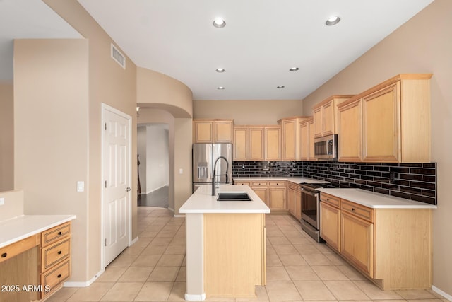 kitchen featuring arched walkways, light brown cabinets, stainless steel appliances, and a sink