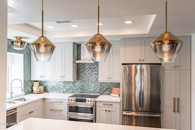 kitchen featuring visible vents, stainless steel appliances, light countertops, wall chimney range hood, and a sink