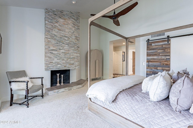 carpeted bedroom with ceiling fan, a barn door, a fireplace, and visible vents