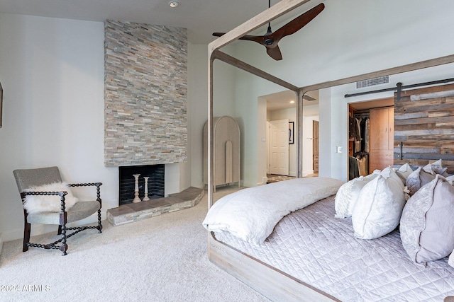 carpeted bedroom featuring a barn door, visible vents, ceiling fan, and a stone fireplace