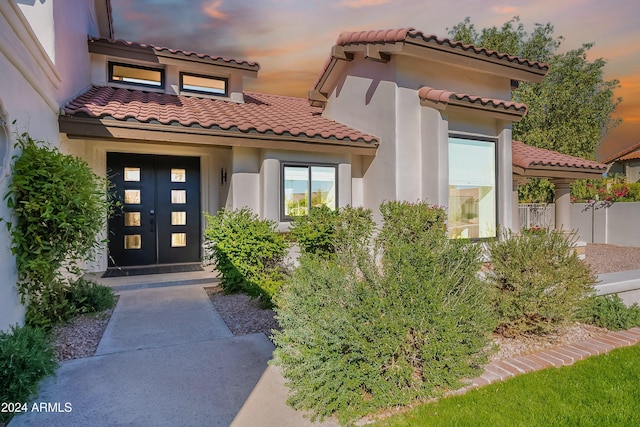 exterior entry at dusk with a tile roof and stucco siding