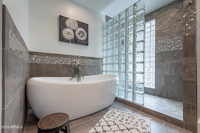 bathroom with a soaking tub, plenty of natural light, tile walls, and tile patterned floors