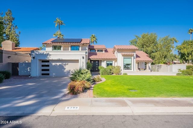 mediterranean / spanish-style home with solar panels, fence, driveway, stucco siding, and a front yard