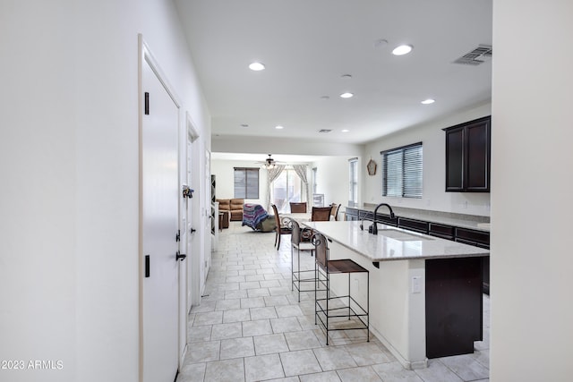 kitchen featuring light stone countertops, a kitchen breakfast bar, ceiling fan, sink, and an island with sink