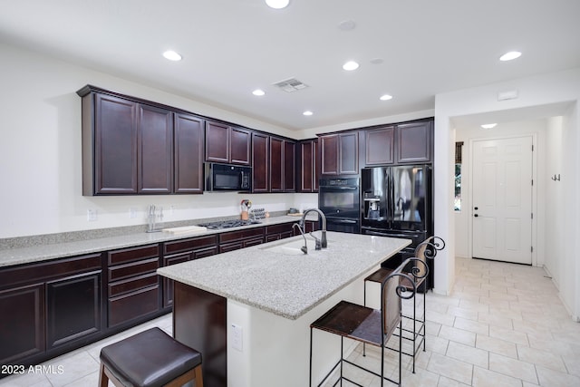 kitchen featuring sink, light stone counters, an island with sink, a breakfast bar area, and black appliances