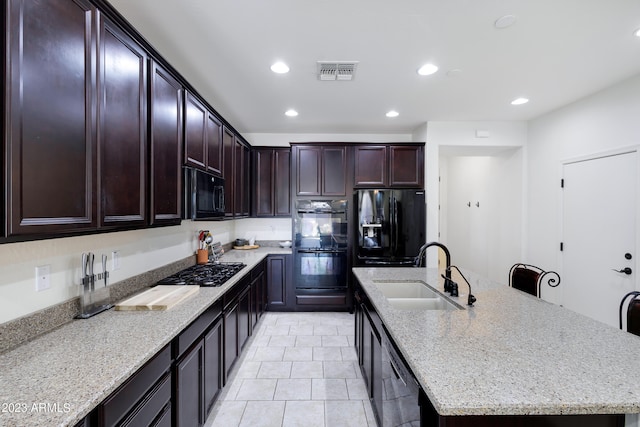 kitchen featuring sink, light stone counters, a center island with sink, light tile patterned flooring, and black appliances