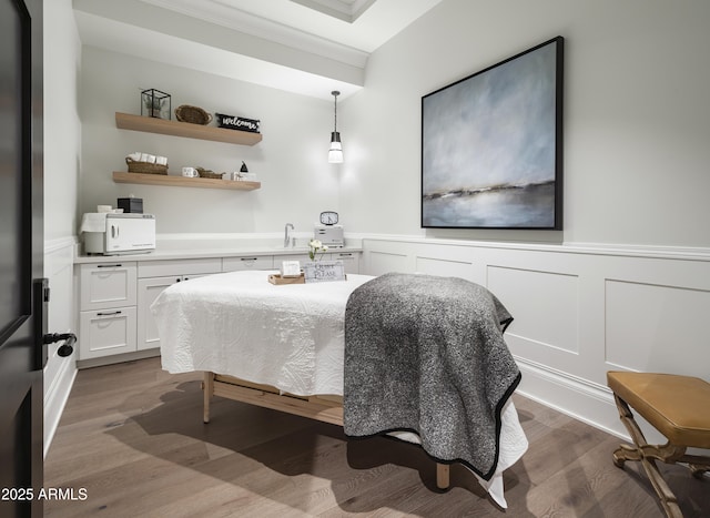 bedroom featuring a decorative wall, wood finished floors, and wainscoting