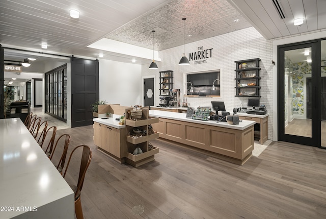 office space with brick wall, a barn door, a raised ceiling, and wood finished floors