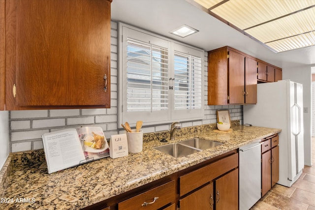 kitchen featuring decorative backsplash, light stone counters, stainless steel dishwasher, sink, and white refrigerator