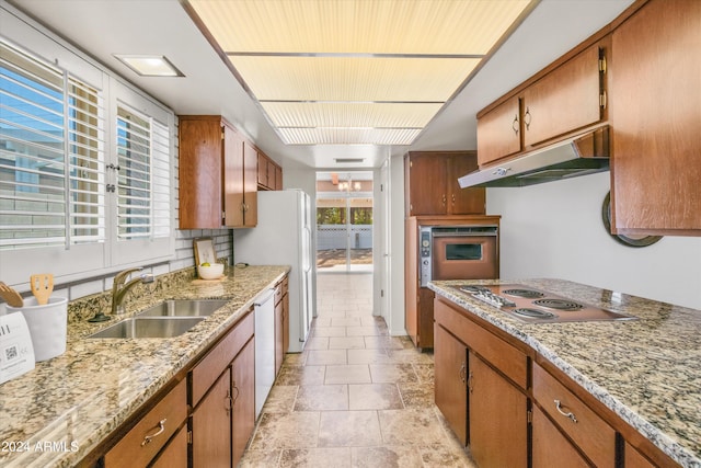 kitchen with light stone countertops, oven, sink, white dishwasher, and electric stovetop