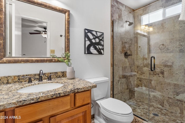 bathroom with toilet, a shower with shower door, vanity, and ceiling fan