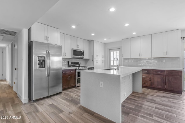 kitchen with a sink, white cabinets, light countertops, appliances with stainless steel finishes, and a center island with sink