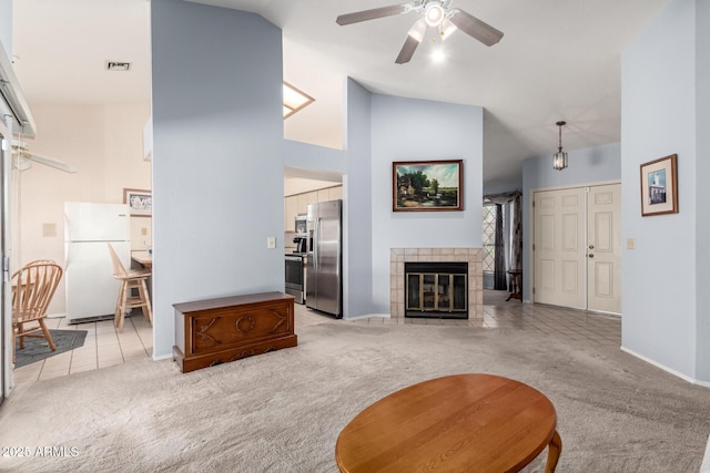 living area featuring visible vents, light carpet, ceiling fan, high vaulted ceiling, and a tile fireplace