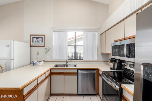 kitchen featuring a peninsula, stainless steel appliances, light countertops, a sink, and light tile patterned flooring