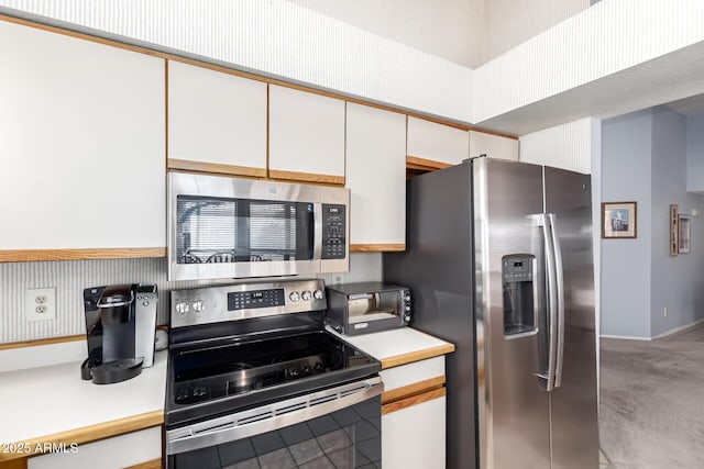 kitchen with light colored carpet, light countertops, appliances with stainless steel finishes, white cabinets, and baseboards