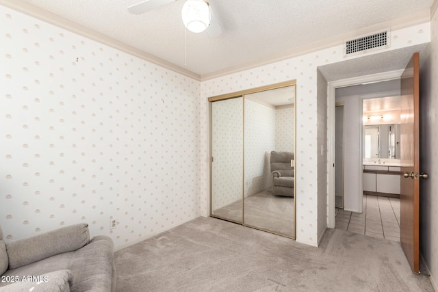 carpeted bedroom featuring wallpapered walls, a closet, visible vents, and a textured ceiling