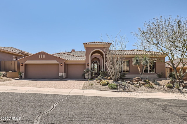 mediterranean / spanish-style house with a tiled roof, driveway, stucco siding, and an attached garage